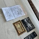 Fotografie zobrazuje příslušenství k hudebnímu nástroji: hridelník basové kytary, uživatelský manuál s nápisem Owners Manual Epiphone, záruční list s…