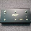 Černý obdélníkový spínací pedalboard s šesti kovovými přepínači. Na povrchu jsou bílé nápisy Rectifier., CH 1, CH 2, CH 3, MUTE, LOOP a SOLO. V dolní…