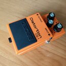 Oranžový efekt pedál s černým gumovým spínacím tlačítkem, na kterém je vyražený nápis BOSS. Na horní části je uveden název Distortion DS-1 a popisky…