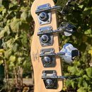 Zadní strana hlavy basové kytary z přírodního dřeva se čtyřmi chromovanými ladičkami. Na dřevě je černý nápis: Designed and backed by Fender® sr 1552…