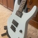 Světle modrá elektrická kytara s tmavým hnedým hmatníkem. Nástroj má tři snímače typu humbucker a jeden ovládací knoflík s nápisem TONE. Povrch kytar…
