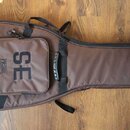 Hnědý polstrovaný obal na kytaru s přední kapsou na zip. Na kapse je bílý nápis SE a vedle něj menší vertikální text PRS GUITARS. Obal je vybaven pop…