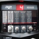 Černý kytarový procesor s nápisem RP155 MODELING GUITAR PROCESSOR. V horní části je červený digitální displej zobrazující číslo 4. Panel obsahuje růz…