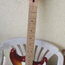 Elektrická kytara s tłem v barvě sunburst a bílým pickguardem. Na hlavě hрифu je nápis Squier STRATOCASTER by Fender. Hриф je vyroben ze světlého dře…