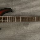 Elektrická basová kytara s trupem v barevném přechodu od žluté přes oranžovou k hnědé a tmavě hnělé. Nástroj má tmavý hnědý pickguard, hnedý hmatník…
