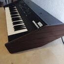 Elektronický klavír v tmavě hnědém dřevěném korpusu s černým ovládacím panelem. Na pravé straně panelu jsou bílé nápisy FARFISA a Synthorchestra 4. N…