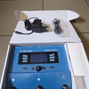 Modrý procesor vokálních efektů v bílé krabici. Na zařízení je nápis TC HELICON a model VoiceLive play. Součástí je napájecí adaptér a kabel v plasto…
