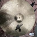 Kruhový činel z kovu s viditelným kování povrchu. Na horní části je nápis „Custom Medium Ride“ a pod ním „22"/56cm“. Ve spodní části je velké černé l…
