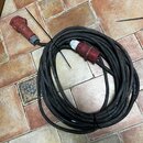 Černý svitek silného elektrického kabelu s červenými konektory na obou koncích. Konektory jsou z plastu a vykazují známky opotřebení v podobě znečišt…