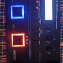 Černý kytarový procesor s nápisy BOSS GT-1 GUITAR EFFECTS PROCESSOR a COSM. Zařízení má tři podsvícená tlačítka (dvě modrá, jedno oranžové) s popisky…