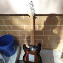 Fotografie zachycuje zadní stranu elektrické kytary s trupem v tmavém sunburst provedení a světlým dřevěným hnedlem. Na zadní straně trupu je vidět k…
