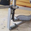 Detailní pohled na kovový pedál basového bubnu v stříbrné barvě. Na povrchu šlapky je viditelný nápis "Savage". Mechanismus obsahuje řetězový pohon a…