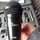 Černý dynamický mikrofon s kovovou mřížkou. Na těle je bílým nápisem uvedena značka "the bone" a model "D1200". Povrch mikrofonu vykazuje mírné známk…