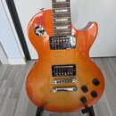 Elektrická kytara s trupem v oranžovo-žlutém sunburst provedení a hnědým hmatníkem s trapezoidními vložkami. Nástroj má dva humbuckery s chromovanými…