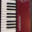 Červený syntetizátor s bílými a černými klávesami. Na červeném povrchu je bílý nápis nord lead 4 performance synthesizer. V pravé části jsou umístěny…