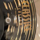 Detailní pohled na černý činel s zlatými nápisy. Je na něm uveden text CLASSIC CUSTOM a 18" Heavy Big Bell Dark Ride. Povrch je zakončen v černé barv…