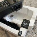 Černý digitální nahrávač s nápisem TASCAM a označením DR-05 LINEAR PCM RECORDER. Vedle něj v bílém polystyrenovém obalu je černý kabel, microSD adapt…