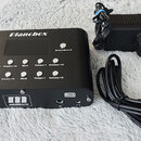 Černý kompaktní modul s nápisem Planobox. Na horní straně se nachází displej, několik tlačítek s popisky (Play/Stop, Drum/Sound, Preset+1, Preset+10,…