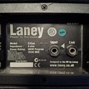 Fotografie zachycuje zadní panel reproduktorového boxu s černým povrchem. Na štítku je bílý nápis Laney a slogan Power To The Music, dále údaje Model…