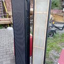 Dvě vysoké, úzké černé reprobedny s kovovými rohy. Levý reproduktor má černou perforovanou mřížku, pravý je zasažen zadu a vidět je na něm světlý dře…