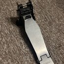 Kovový pedál s černým plastovým mechanismem, položený na hnědém koberci. Na spodní části stříbrného šlapáku je vyryté logo Roland. Povrch kovové část…