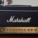 Kytarový zesilovač značky Marshall v černém texturovaném potahu s bílým lemováním mřížky. Zlatý ovládací panel obsahuje nápisy MASTER, REVERB, EQUALI…