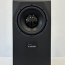 Černý studiový subwoofer v hranatém korpusu s matným povrchem. Na přední straně je umístěn velký kruhový reproduktor a pod ním ovládací panel s nápis…