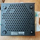 Spodní strana šedého audio rozhraní s černým kovovým dnem a perforovaným chladicím otvorem. V dolní části je bílý štítek s nápisy „UAD 2“, „Apollo Tw…