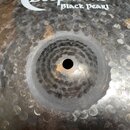 Detailní pohled na tmavý, kovaný činel s výraznou texturou v podobě drobných důlků po celém povrchu. V horní části je bílý nápis Black Pearl. Povrch…