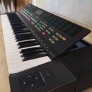 Černý digitální klavír s bílými a černými klávesami. Na horním ovládacím panelu je nápis ESP-2000, displej a řada tlačítek v různých barvách. V pravé…