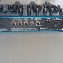 Zadní strana modrého efektového procesoru s několika vstupy a výstupy. Na šasi jsou viditelné nápisy INPUT, GUITAR AMP. R, GUITAR AMP. L (MONO), LINE…