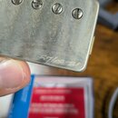 Detail kovového snímače s четыřmi viditelnými šrouby. Povrch kovu je matný, s viditelným opotřebením a oxidací. V dolní části je vyryt nápis 57/08 TM.