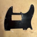 Černý plastový pickguard pro elektrickou kytaru s výřezem na snímač. Povrch vykazuje viditelné množství drobných škrábanců a známky opotřebení. Na dí…