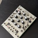 Stříbrný modul syntetizátoru s nápisem MATHS a logem MAKENOISE. Přední panel obsahuje dvanáct černých otočných potenciometrů, několik bílých tlačítek…