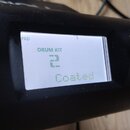 Detailní záběr na displej elektronického bicího modulu v černém plastovém rámu. Na bílém displeji je zelený nápis DRUM KIT, pod ním číslice 2 a dále…