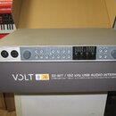 Stříbrná USB audio rozhraní v kartonové krabici. Na předním panelu jsou dva vstupy, několik ovládacích knoflíků a řada tlačítek s nápisy jako INST 1/…