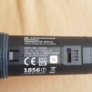 Detailní záběr na černý ruční vysílač s nálepkou s technickými údaji. Na štítku je logo a nápis SENNHEISER, dále text HANDHELD TRANSMITTER SKM 35 a F…