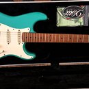 Tyrkysová elektrická kytara typu Stratocaster s bílým pickguardem a hnědým hmatníkem v černém kufru. Na hlavě kytary je viditelné logo Xotic. Vedle n…