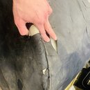 Detailní záběr na černý textilní obal nebo pouzdro. Materiál je viditelně opotřebovaný, znečištěný a v horní části vytrhaný, skrz který je vidět svět…