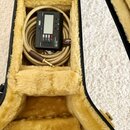 V plyšovém pouzdře je srolovaný béžový kabel s hnědým konektorem. Na kabelu je připevněn černý ladička s displejem a nápisy KORG, GA-50 a GUITARIST T…