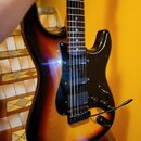 Elektrická kytara s trupem v barevném přechodu od žluté přes oranžovou k černému. Má černý pickguard, tři snímače a černý most s pákou vibrata. Na sn…