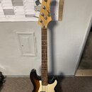 Elektrická basová kytara s trupem v tmavém sunburst provedení a bílým pickguardem. Na hlavě hmatníku je viditelné logo Cort. Nástroj má hnědý dřevěný…