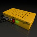 Žlutý kovový box s ventilačními otvory na horní straně. Na přední straně jsou umístěny dva konektory s připojenými kabely, jeden přepínač, červený vy…