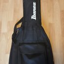 Černý softcase na kytaru s bílým nápisem Ibanez v horní části. Pouzdro má v přední části velkou kapsu na zip a ramenní popruhy. Povrch vykazuje mírné…