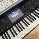 Černý digitální klavír s bílými a černými klávesami. Na displeji je vidět logo KORG a nápis KRONOS MUSIC WORKSTATION. Povrch nástroje obsahuje různé…