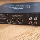 Černý audio rozhraní Focusrite s kovovým povrchem. Na zadní straně jsou viditelné konektory USB 2.0, MIDI OUT, MIDI IN a LINE OUTPUTS s označením -10…