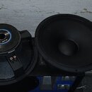 Dva černé reproduktory, z nichž jeden je zobrazen zepředu a druhý zezadu. Na zadní straně levého reproduktoru je vidět modro-bílá nálepka s nápisem "…