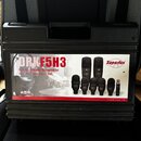 Černý plastový kufřík s rukojetí a uzavíracími zámky. Na přední straně je nalepená štítková etiketa s nápisy DRKF5H3, Drum Kit/Instrument Microphone…