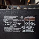 Záběr na zadní stranu černého kytarového komba s texturavaným povrchem. Na kovovém štítku je uveden model HOT ROD Deluxe TM IV, výrobce FENDER MUSICA…