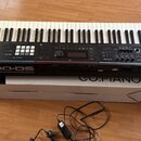 Černý digitální klavír s bílými a černými klávesami. Na přední hraně je bílý nápis Roland JUNO-DS. Nástroj leží na bílé krabici s nápisy GO-61P a GO:…